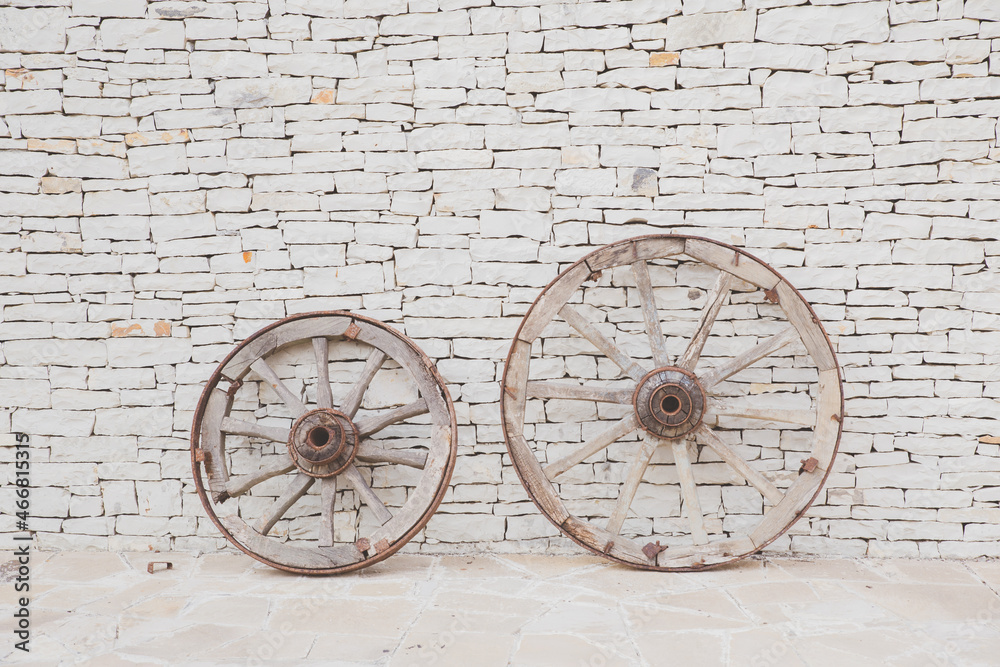 Two vintage wooden wheels. Antique masonry in beige shades. Beautiful textured background from natural stone. Hand laid sandstone or shell rock wall. Symbol of energy, life cycle, movement.
