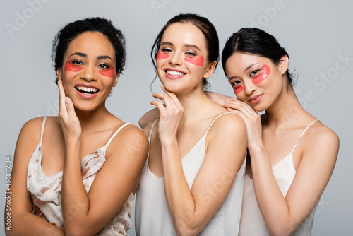Positive interracial women with eye patches posing and looking at camera isolated on grey