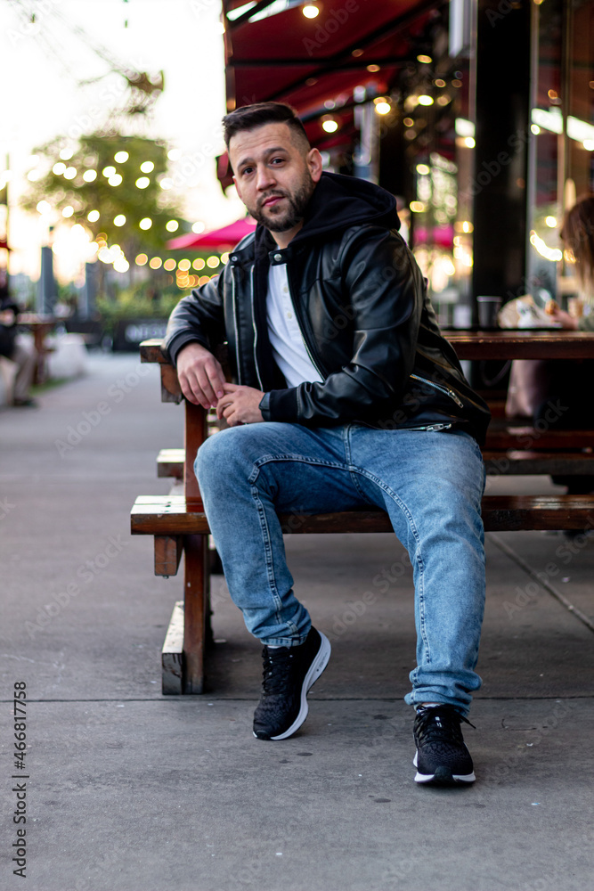happy man with beard and leather jacket posing outdoors sitting in a restaurant