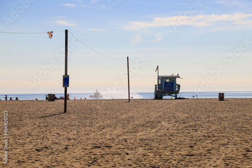 people walking and relaxing on the beach with silky brown sand, vast blue ocean water along the pier and lifeguard towers with blue sky at Santa Monica Beach in California USA