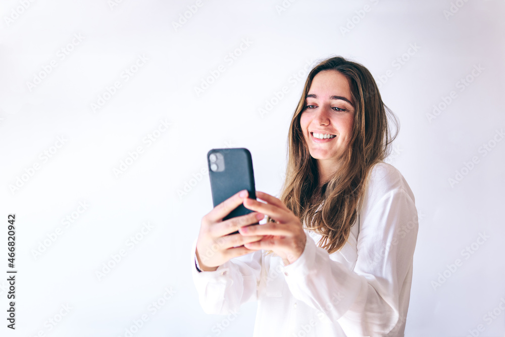 Young woman looking at her mobile phone on grey background. Concept of online social networks Young woman looking at her mobile phone on grey background. Concept of online social networks