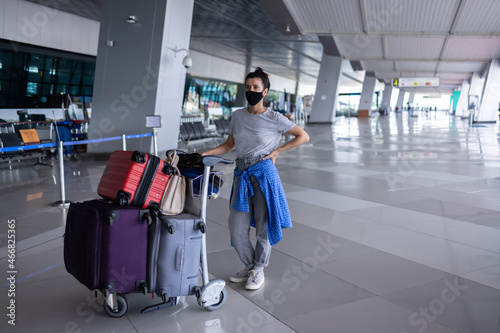 Canvas-taulu Young woman with face mask standing at airport terminal pushing luggage trolley with many bags before check in