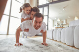 Portrait of smiling father exercising while holding daughter and son on his back during workout indoors