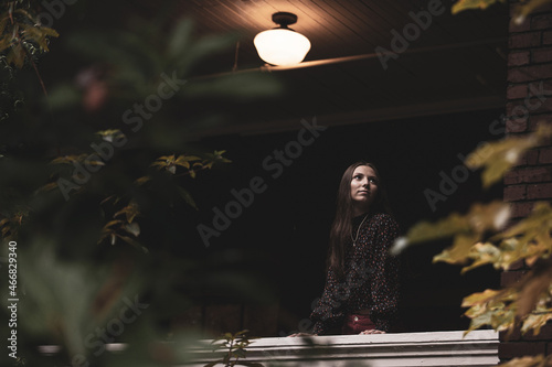 Portrait of young woman standing under a light fixture on an old home patio