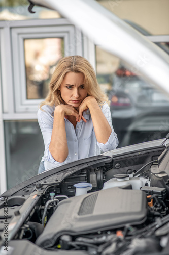Pensive woman looking sadly into open hood of car
