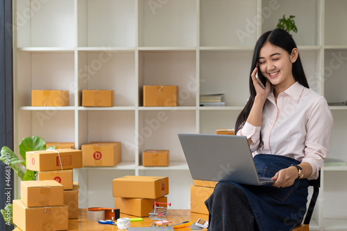 Young Asian woman, entrepreneur, a business owner who works with computers at home. Online shopping delivery, SME small business entrepreneur or independent Asian woman working with boxes. © ArLawKa