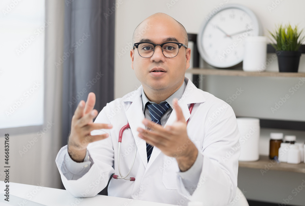 Young asian man doctor works from home working online looking and camera talking with patient Explain about taking medications to treat illnesses.