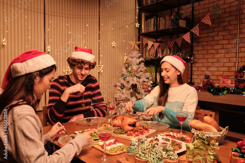 Friends enjoy fun eating diner at table with specials foods  young woman cutting roasted turkey at home s dining room  decorated with ornaments  Christmas festival  and New Year celebration party.