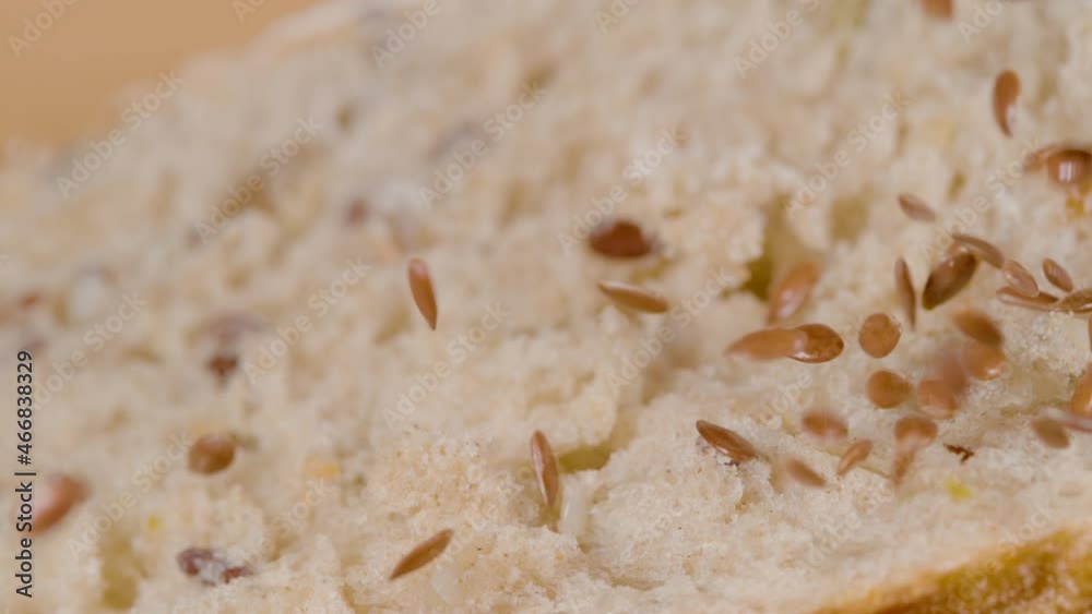 SLOW MOTION, MACRO, DOF: Linseeds get scattered on top the crumb of a freshly baked homemade whole wheat bread. Shiny red and brown colored linseeds fall on the rustic loaf of bread cut in half. SLOW MOTION, MACRO, DOF: Linseeds get scattered on top the crumb of a freshly baked homemade whole wheat bread. Shiny red and brown colored linseeds fall on the rustic loaf of bread cut in half.