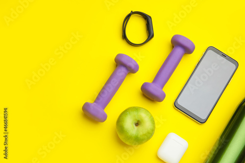 Dumbbells, gadgets and apple on yellow background