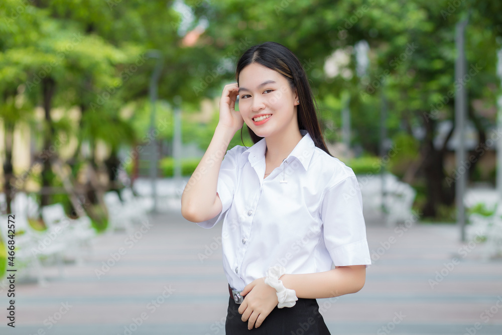 Young Asian woman student who has blond long hair smiles and looks at to camera while holding hands and standing in university with outdoor garden tree background. Young Asian woman student who has blond long hair smiles and looks at to camera while holding hands and standing in university with outdoor garden tree background.