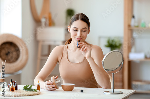 Young woman sitting at table and smelling natural essential oil in bottle photo