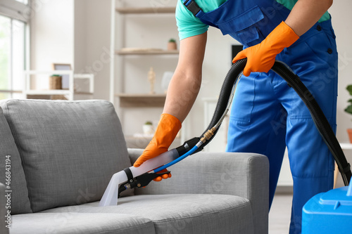 Male worker removing dirty stain from grey sofa with vacuum cleaner in room Fotobehang