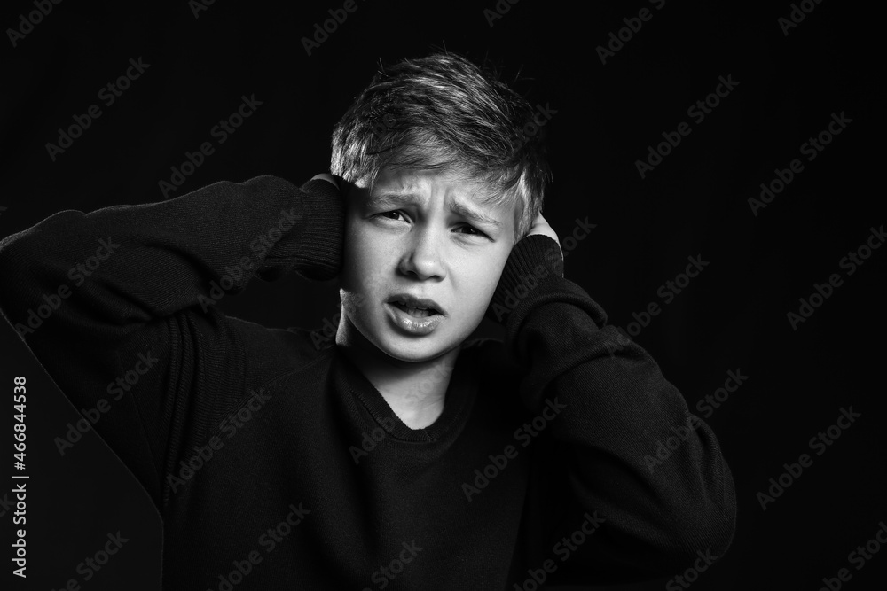 Upset little boy closing ears on black background Upset little boy closing ears on black background