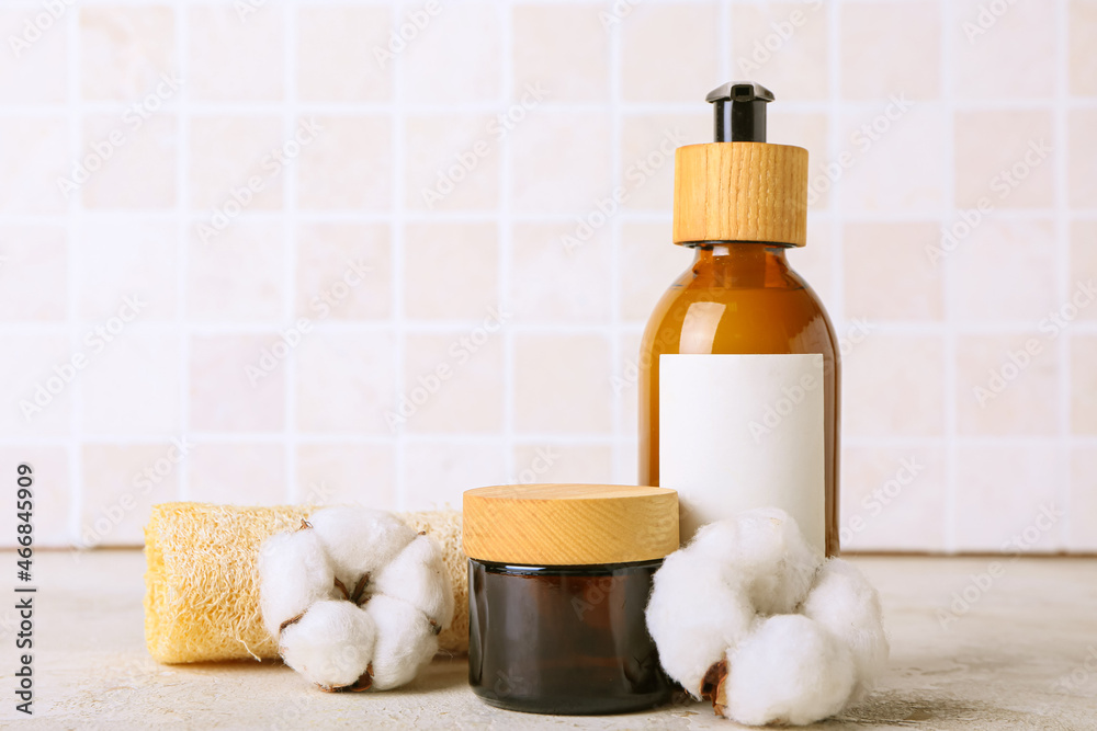 Cosmetic products, sponge and cotton flowers on table against tile wall Cosmetic products, sponge and cotton flowers on table against tile wall