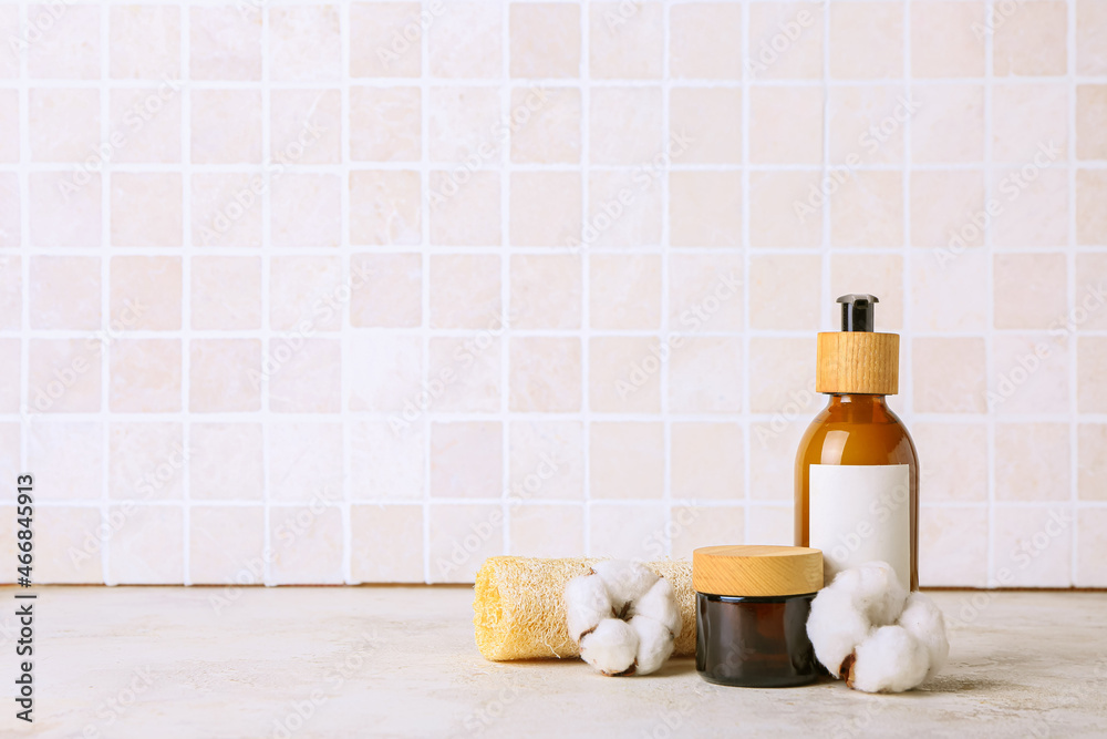 Cosmetic products, sponge and cotton flowers on table against tile wall Cosmetic products, sponge and cotton flowers on table against tile wall