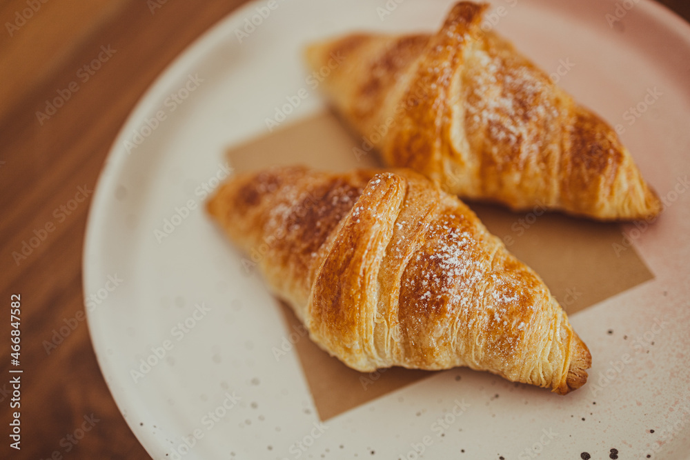 Two appetizing croissants on a plate are placed on a wooden table in the cafe.