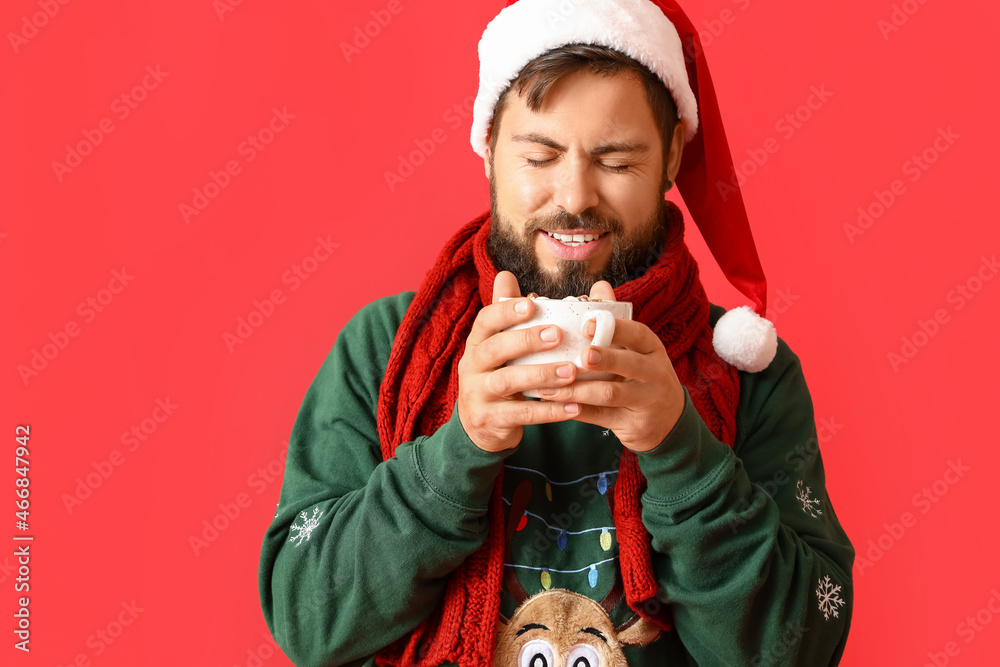 Handsome man in Santa hat with cup of hot cocoa on red background Handsome man in Santa hat with cup of hot cocoa on red background