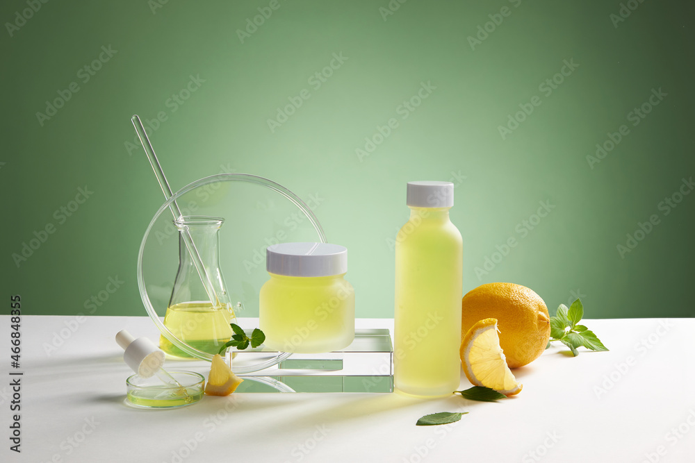 Fototapeta premium Lemon extract with transparent podium with test tube in green background , green leaf , sliced lemon for advertising , frontview , photography experiment concept