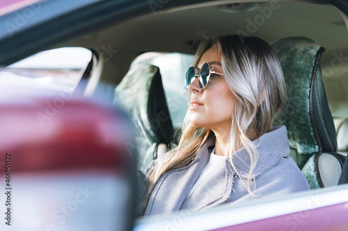 Young stylish woman with long blonde hair and sunglasses driving car