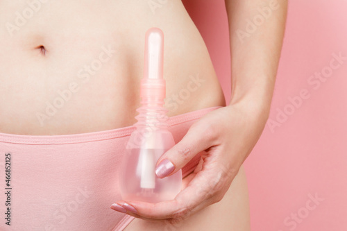 Concept of Gynecology, woman health. Vaginal enema in woman's hand on pink background near her body. Treatment of vaginal infections from candidiasis, thrush, sexually transmitted infections photo