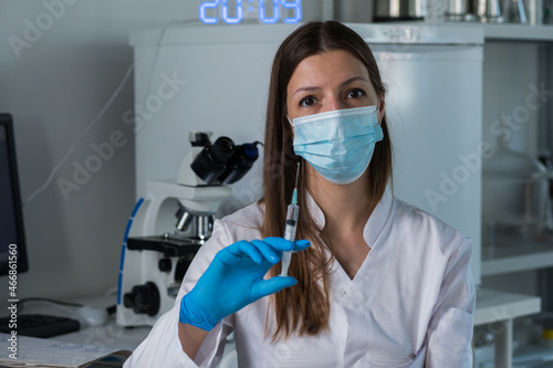 Female doctor with medical mask and gloves prepares prefilled syringe for injection by removing cap