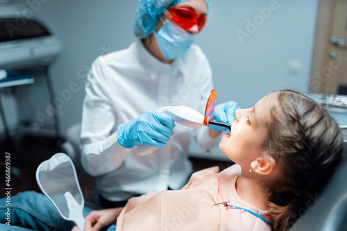 woman dentist providing tooth restoration and filling with curing polymerization UV lamp for child