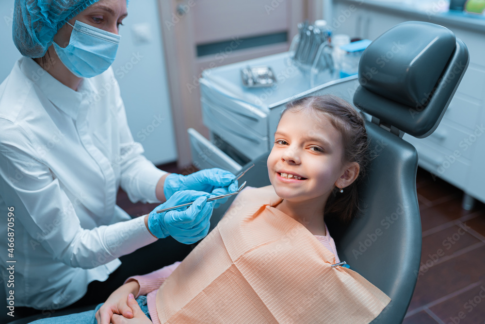 Cute young girl visiting dentist, having his teeth checked by female dentist in dental office