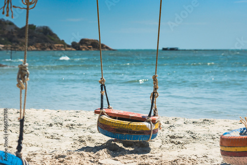 Copy space Hang rope swing old tires paint orange blue yellow. Nature sand beach bright sea horizon skyline island background. Day sun summer joy fun. Paradise sea vacation. Beauty romantic landscape