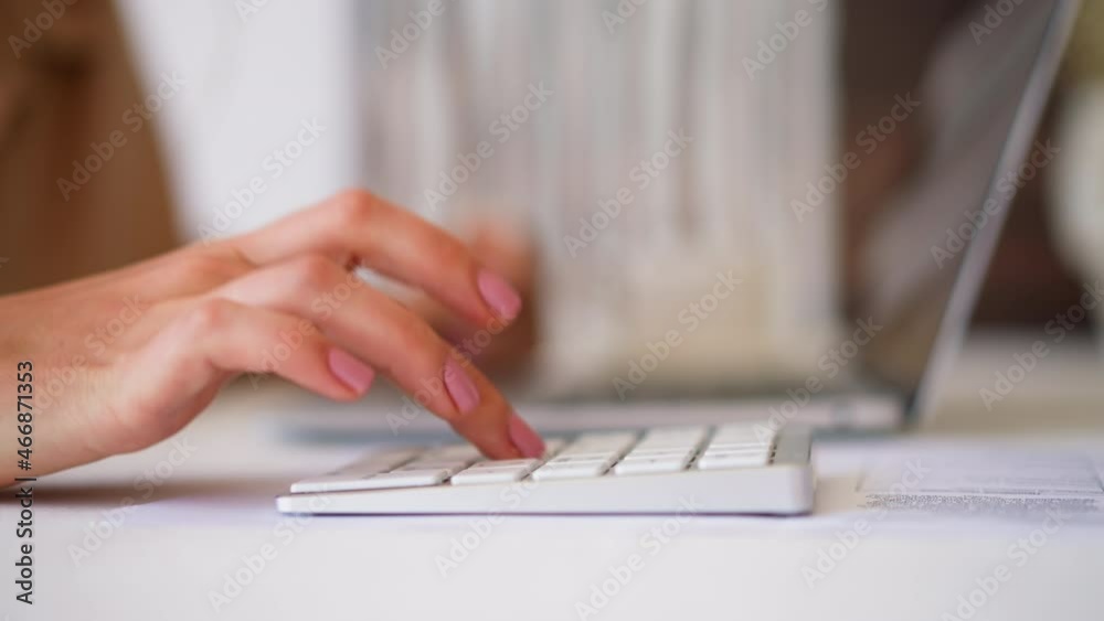 Woman hand makes calculations typing on modern white numeric keyword and laptop against blurred background in office slow motion extreme closeup Woman hand makes calculations typing on modern white numeric keyword and laptop against blurred background in office slow motion extreme closeup