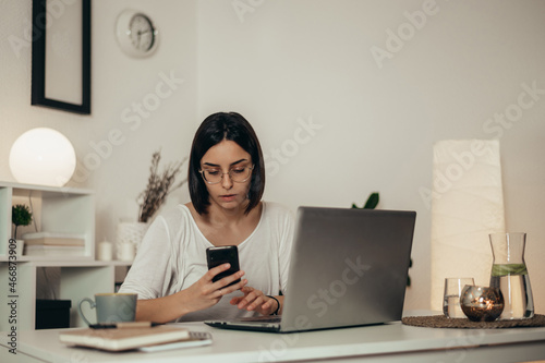 Beautiful woman using smartphone and a laptop while working from home