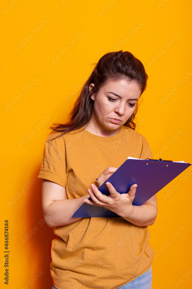 Young person taking notes on notebook files with pen in studio. Concentrated woman writing on textbook papers, signing documents and paperwork about project on notepad clipboard. Young person taking notes on notebook files with pen in studio. Concentrated woman writing on textbook papers, signing documents and paperwork about project on notepad clipboard.