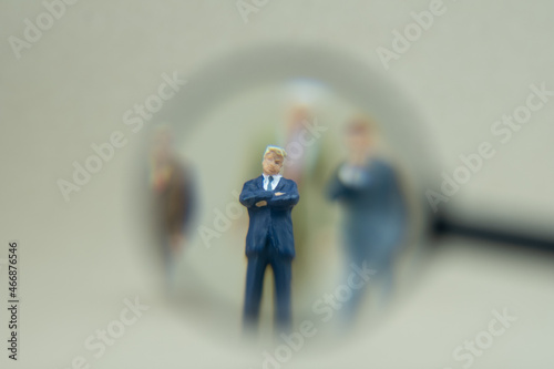 Miniature people in magnifying glass focusing on businessman