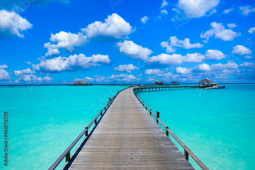 Calm meditational ocean lagoon with blue sunny sky. Idyllic natural view with long wooden jetty into paradise island, luxury travel destination. Inspirational scenic view, Maldives freedom vacation