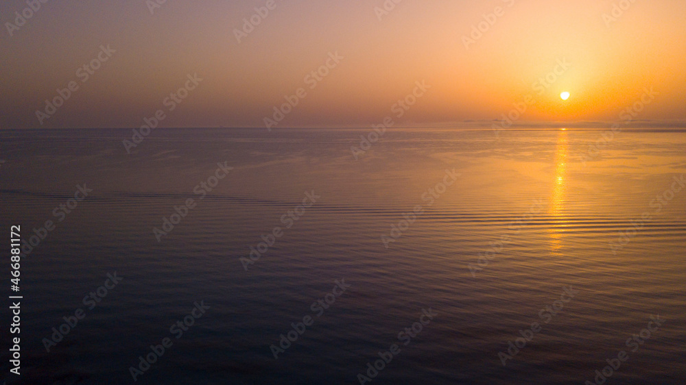 Obraz premium Peaceful seascape landscape aerial view of calm ocean sea water during sunset or sunrise time. Orange and colorful sky and waves. Travel destination amazing place and moments concept
