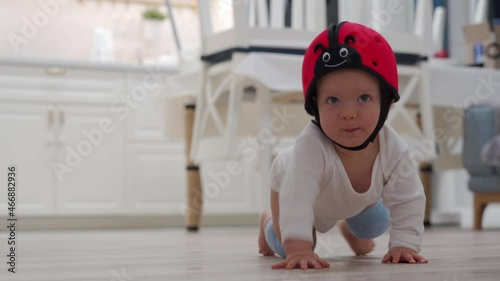 Cute baby wearing safety helmet and knee pads for crawling learning to crawl on the floor at home, 7 month old caucasian toddler exploring all around the house. High quality 4k footage