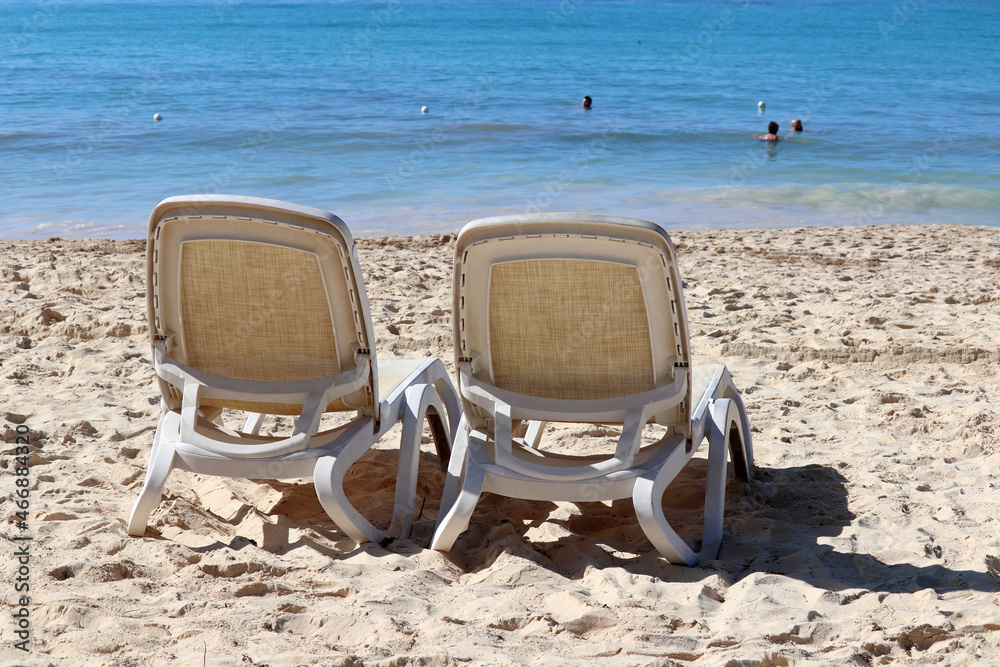Sea sandy beach with two empty deck chairs on swimming people background. Vacation on tropical resort Sea sandy beach with two empty deck chairs on swimming people background. Vacation on tropical resort