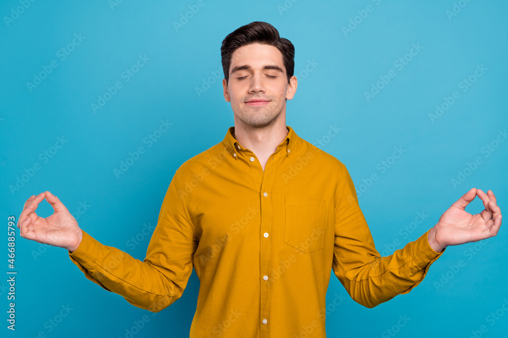 Photo of serene peaceful guy hold fingers meditate yoga wear yellow shirt isolated blue color background Photo of serene peaceful guy hold fingers meditate yoga wear yellow shirt isolated blue color background