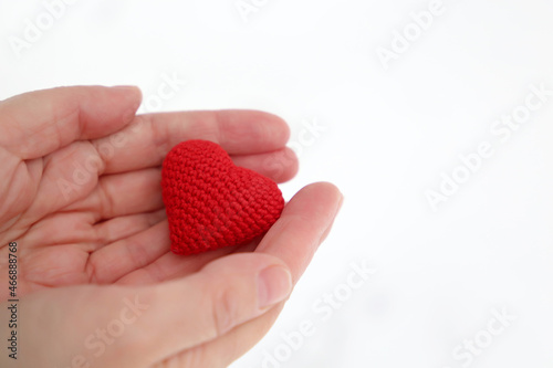 Red knitted heart in female palms of hands against the white snow. Concept of a romantic love, Valentine's day or charity