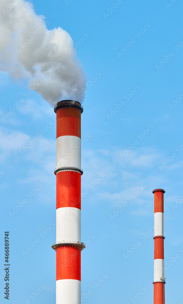 Red and white painted smoking chimneys against the blue sky. Red and white painted smoking chimneys against the blue sky.