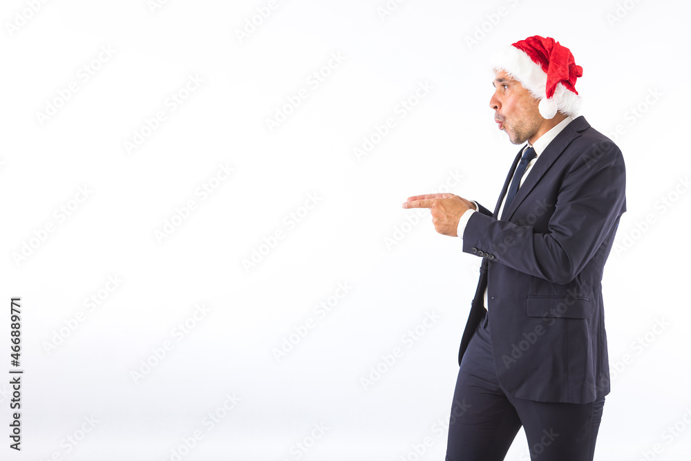 Businessman dressed in suit, tie and Christmas hat of Santa Claus, surprised, pointing with his hands, on white background. Christmas celebration concept. Businessman dressed in suit, tie and Christmas hat of Santa Claus, surprised, pointing with his hands, on white background. Christmas celebration concept.