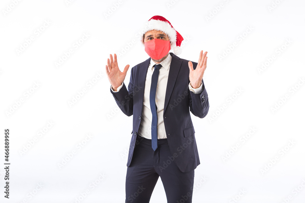 Businessman dressed in suit, tie, Santa Claus Christmas hat and red mask, raising hands having fun, on white background. Christmas celebration concept. Businessman dressed in suit, tie, Santa Claus Christmas hat and red mask, raising hands having fun, on white background. Christmas celebration concept.