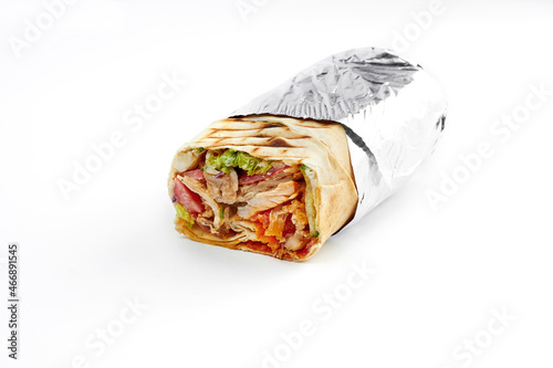 Large shawarma with meat and vegetables, wrapped in foil on a white background. Close-up, selective focus