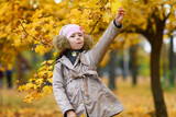 Portrait of a girl in an autumn park. The child is standing near a beautiful maple tree with yellow leaves. Beautiful nature