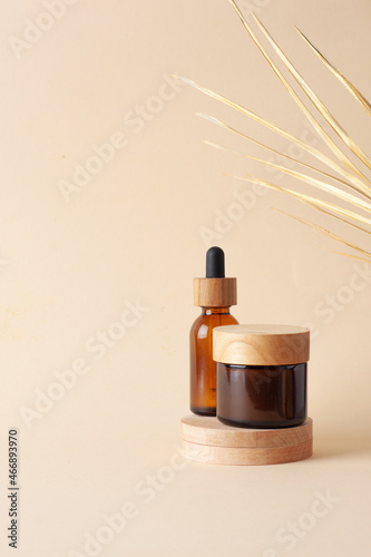 Cosmetic skin care products with wood podium and palm leaf on pastel beige background. Close up, copy space