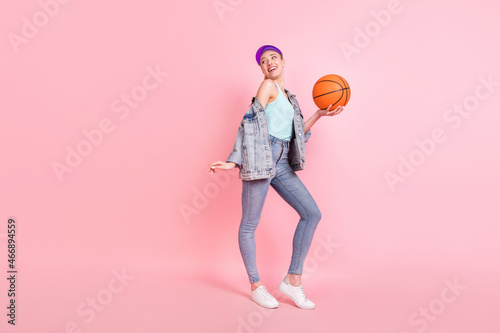 Full size profile photo of funny sporty lady hold ball look empty space wear jeans shirt cap isolated on pink background
