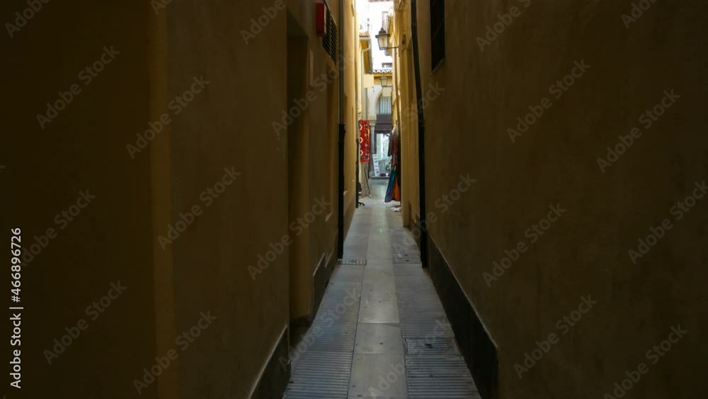 Dark narrow alley in the historical centre of Granada, Andalusia, Spain. Dark walls on both sides. Commercial street at the vanishing point. Dark narrow alley in the historical centre of Granada, Andalusia, Spain. Dark walls on both sides. Commercial street at the vanishing point.