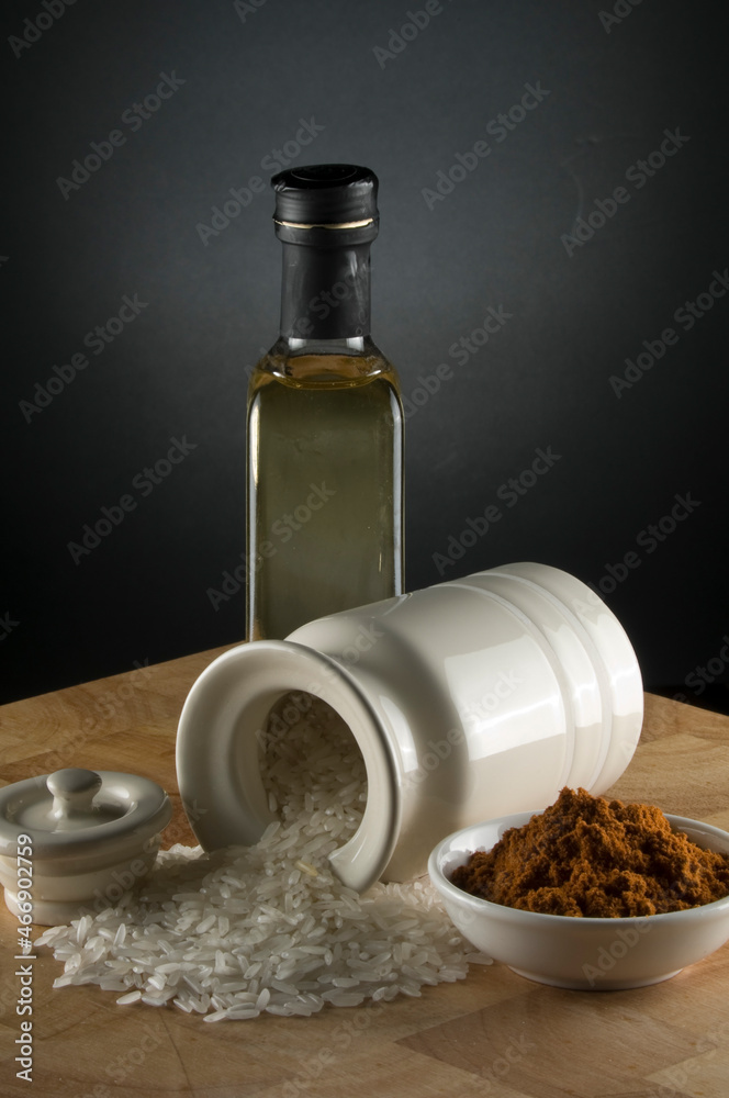 Olive oil bottle with paprika in bowl and rice spilling out of white canister on timber bench Olive oil bottle with paprika in bowl and rice spilling out of white canister on timber bench