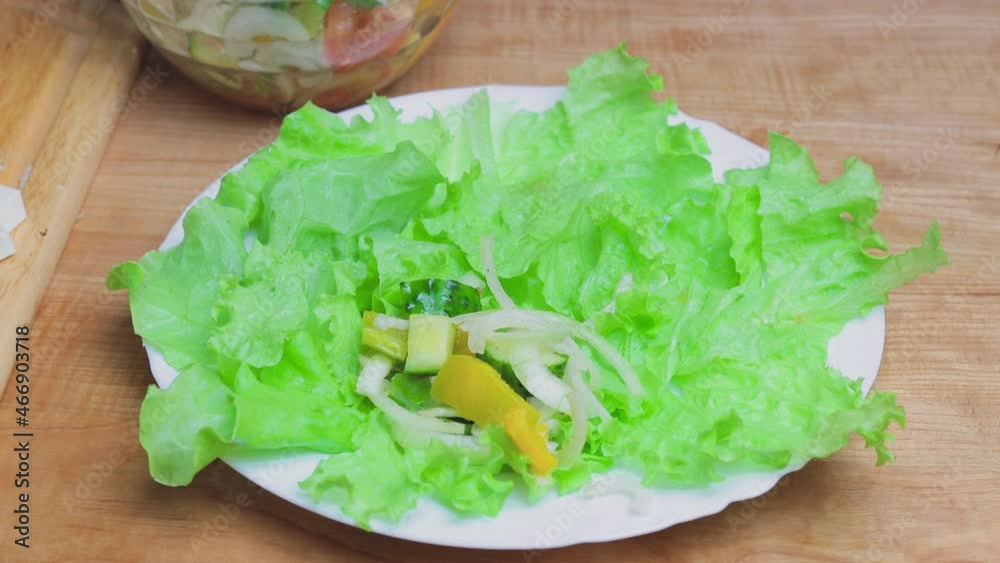 Putting fresh vegetable greek salad on a plate with green lettuce leaves, vegetarian food Putting fresh vegetable greek salad on a plate with green lettuce leaves, vegetarian food
