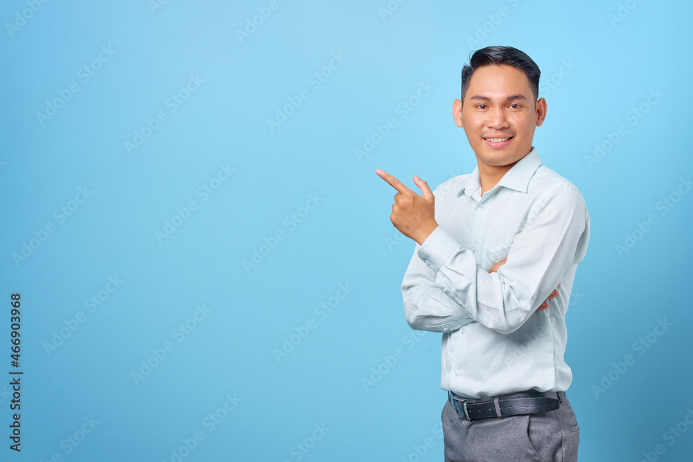 Smiling young handsome businessman pointing finger away at copy space on blue background Smiling young handsome businessman pointing finger away at copy space on blue background